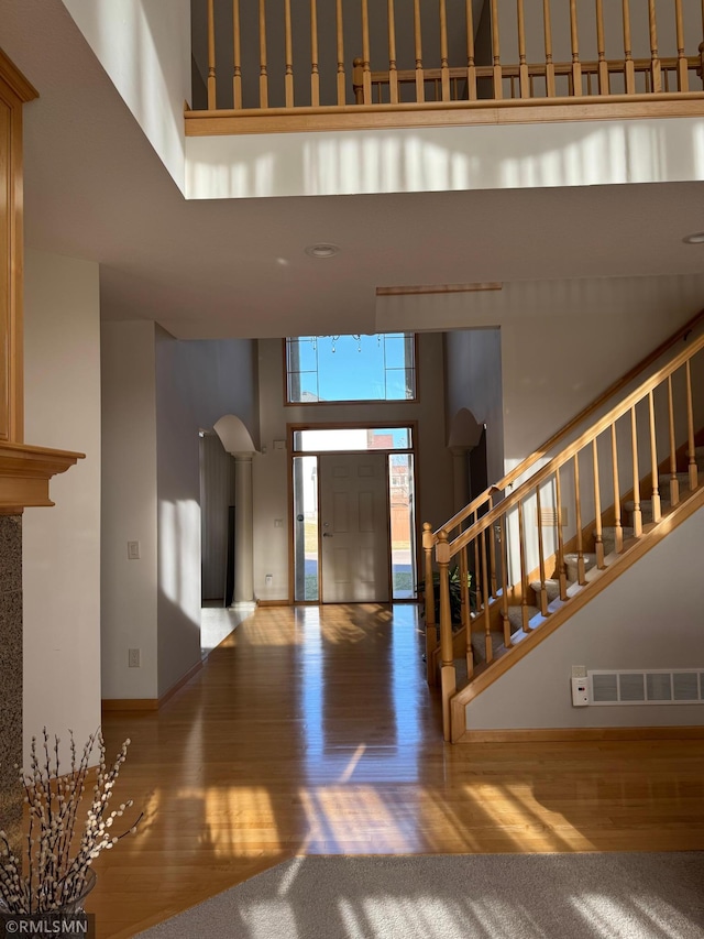 foyer entrance with visible vents, baseboards, wood finished floors, a high ceiling, and stairway