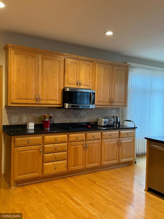 kitchen featuring recessed lighting, stainless steel appliances, backsplash, dark stone counters, and light wood-style flooring