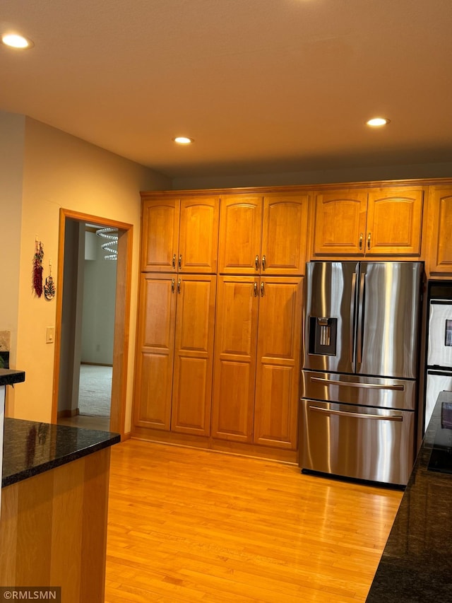 kitchen featuring brown cabinets, appliances with stainless steel finishes, dark stone countertops, and light wood-style flooring