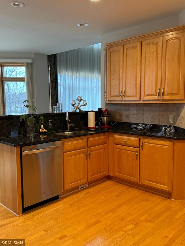 kitchen with a sink, dark stone counters, light wood-style floors, decorative backsplash, and dishwasher
