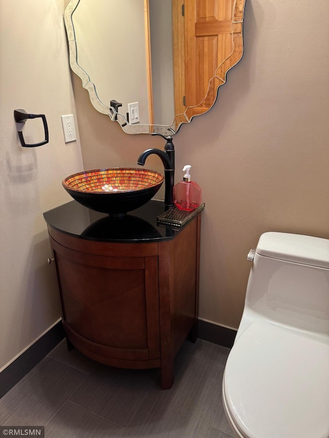 half bath with baseboards, vanity, and toilet