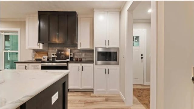 000 Pine Ave S, Sandstone, MN 55072 - kitchen featuring stainless steel microwave, light wood-style floors, white cabinets, decorative backsplash, and ornamental molding