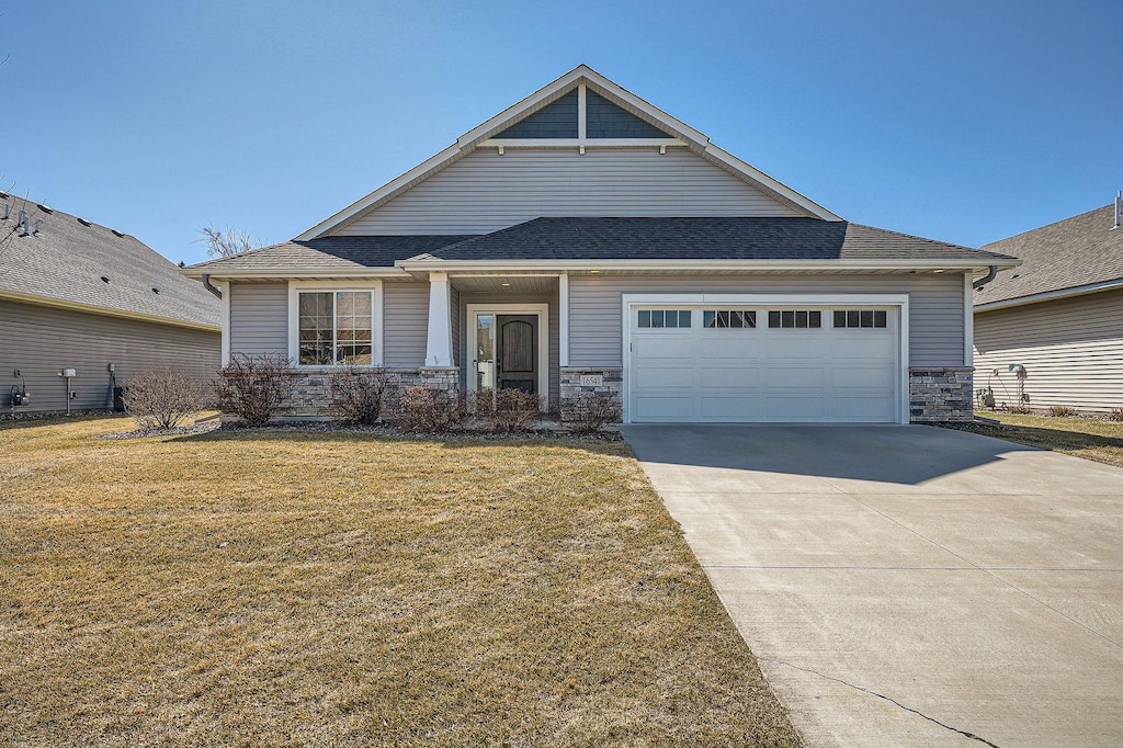 view of front of home with roof with shingles, concrete driveway, a front yard, and stone siding