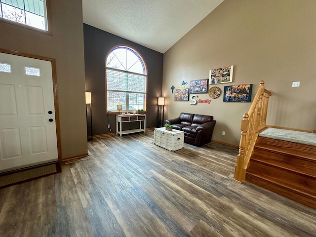 entryway with a wealth of natural light, high vaulted ceiling, stairs, and dark wood-style floors