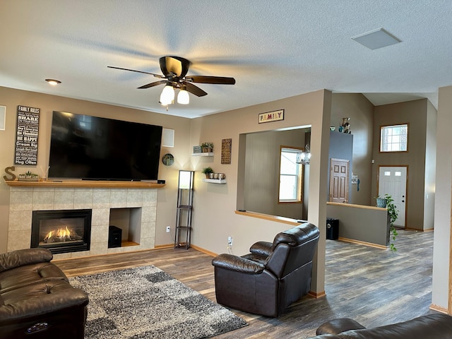 living area with wood finished floors, a ceiling fan, baseboards, a tiled fireplace, and a textured ceiling