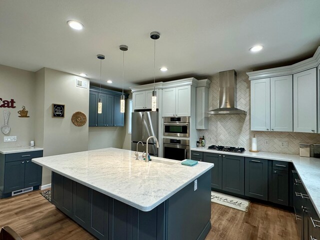 kitchen featuring wall chimney exhaust hood, a sink, dark wood-style flooring, decorative backsplash, and appliances with stainless steel finishes