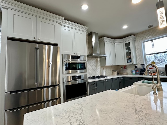 kitchen with stainless steel appliances, a sink, wall chimney exhaust hood, decorative backsplash, and glass insert cabinets