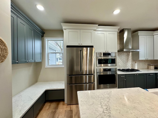 kitchen featuring light stone countertops, wall chimney range hood, light wood finished floors, and stainless steel appliances