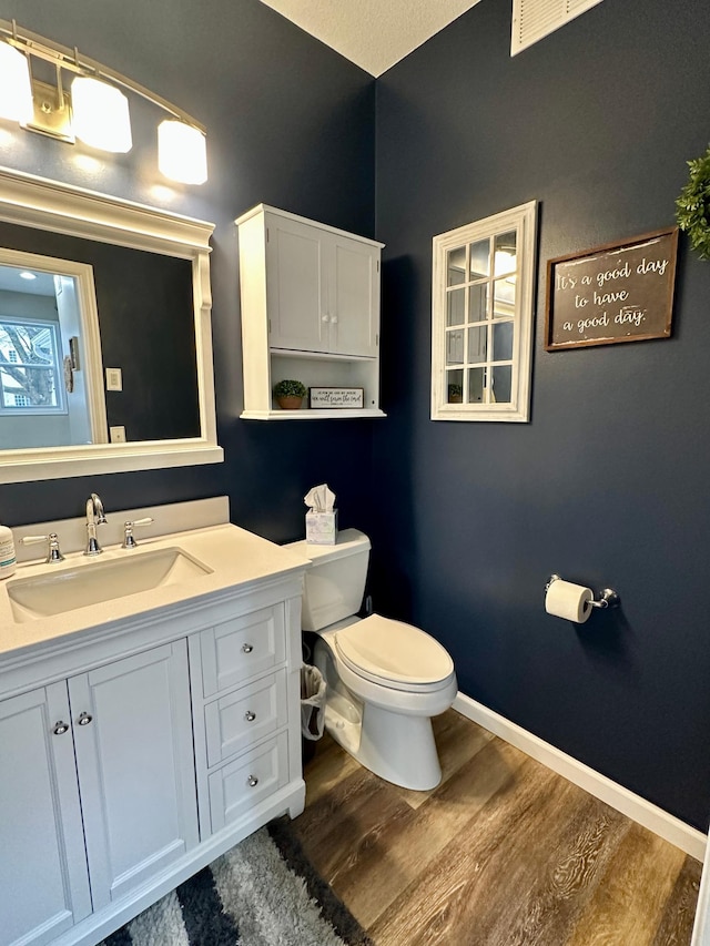 bathroom featuring baseboards, wood finished floors, toilet, and vanity