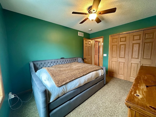 carpeted bedroom with ceiling fan, a textured ceiling, visible vents, and a closet