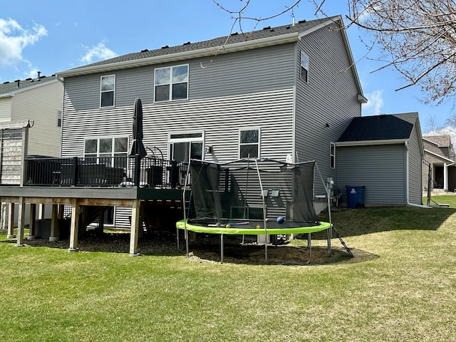 back of property with a wooden deck, a yard, and a trampoline