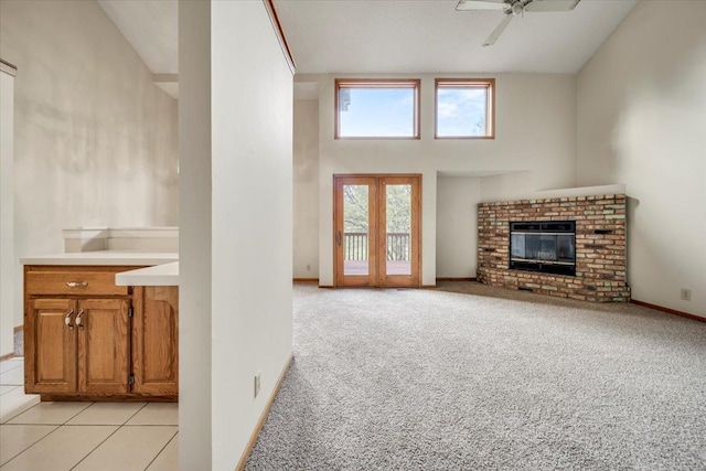 unfurnished living room featuring light carpet, baseboards, a towering ceiling, ceiling fan, and a fireplace