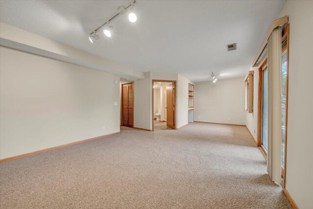 spare room featuring baseboards, visible vents, rail lighting, and light colored carpet
