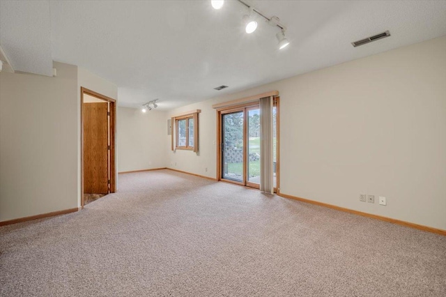 carpeted spare room featuring rail lighting, baseboards, and visible vents