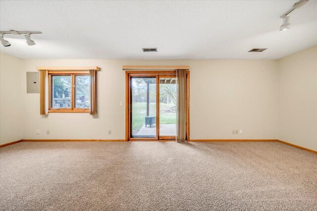 carpeted empty room with track lighting, baseboards, visible vents, and electric panel