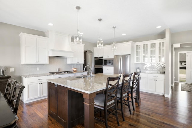 kitchen featuring a sink, arched walkways, dark wood finished floors, stainless steel appliances, and tasteful backsplash