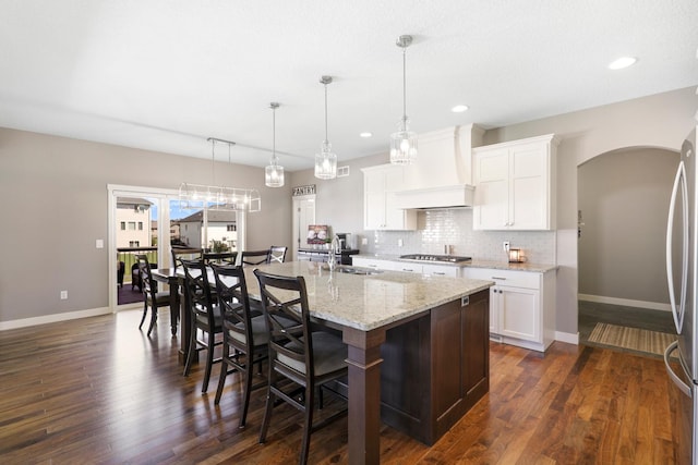 kitchen featuring backsplash, a sink, premium range hood, stainless steel appliances, and an island with sink