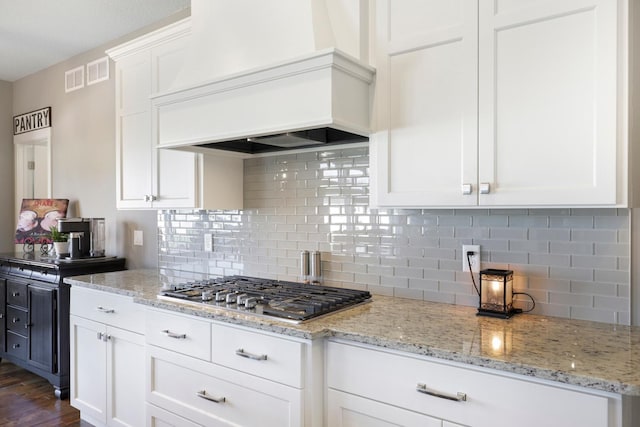 kitchen featuring stainless steel gas cooktop, white cabinetry, backsplash, and premium range hood