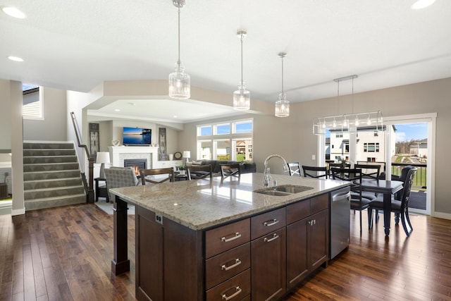 kitchen with a breakfast bar area, a lit fireplace, dark wood-type flooring, a sink, and hanging light fixtures