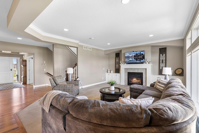 living room featuring visible vents, a tile fireplace, baseboards, ornamental molding, and stairs