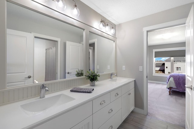 ensuite bathroom with double vanity, baseboards, a sink, and a textured ceiling