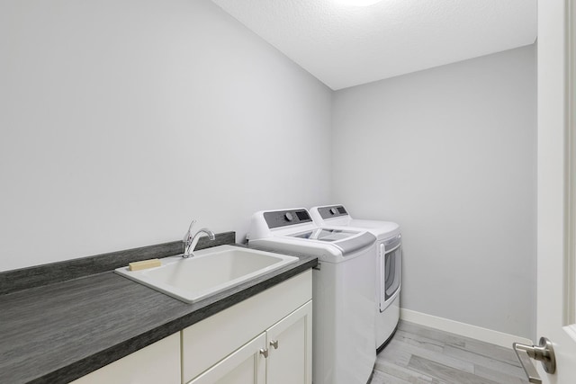 laundry area featuring washer and dryer, light wood-style floors, baseboards, a sink, and cabinet space