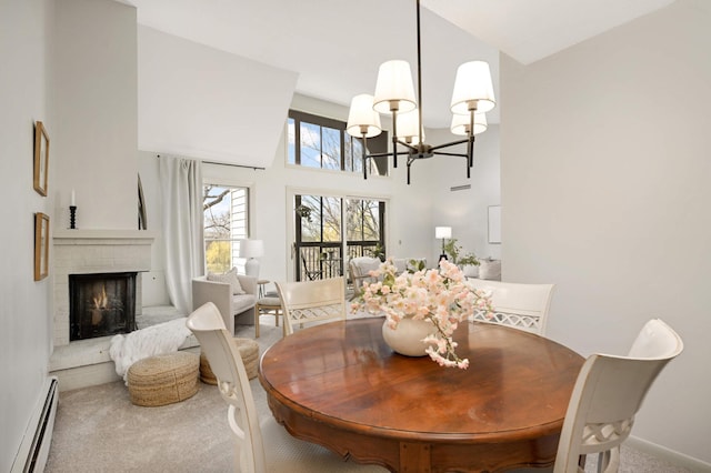 dining space featuring baseboard heating, an inviting chandelier, a towering ceiling, carpet, and a brick fireplace