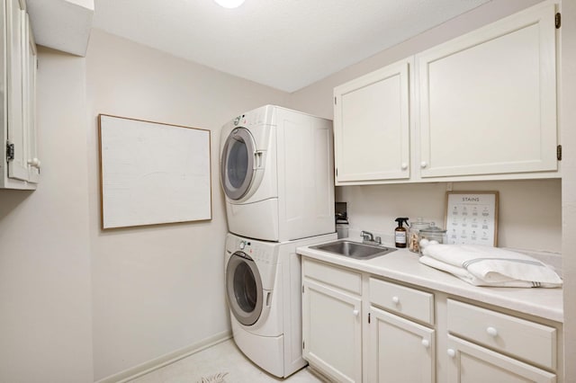 clothes washing area featuring baseboards, cabinet space, stacked washer and dryer, and a sink