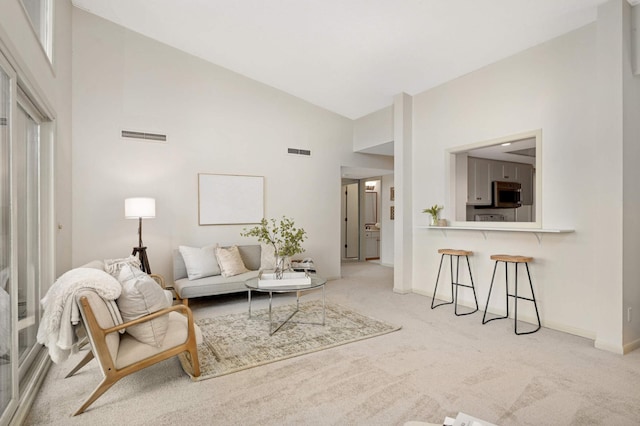 living area with light carpet, baseboards, visible vents, and high vaulted ceiling