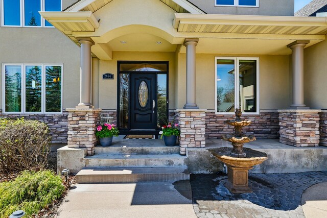 entrance to property featuring covered porch, stone siding, and stucco siding