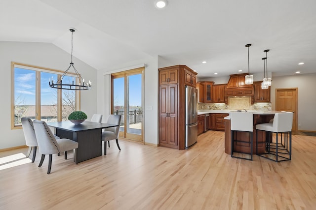 kitchen with a wealth of natural light, custom exhaust hood, a chandelier, and stainless steel refrigerator