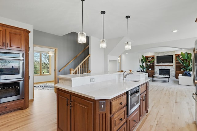 kitchen with brown cabinetry, light stone countertops, double oven, a sink, and light wood-style flooring