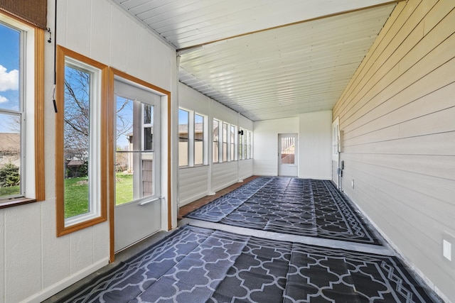 unfurnished sunroom featuring plenty of natural light, baseboards, and wooden walls