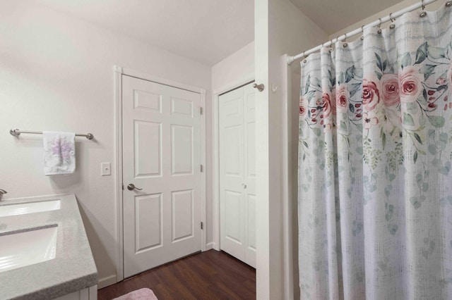 bathroom featuring a shower with shower curtain, double vanity, wood finished floors, and a sink