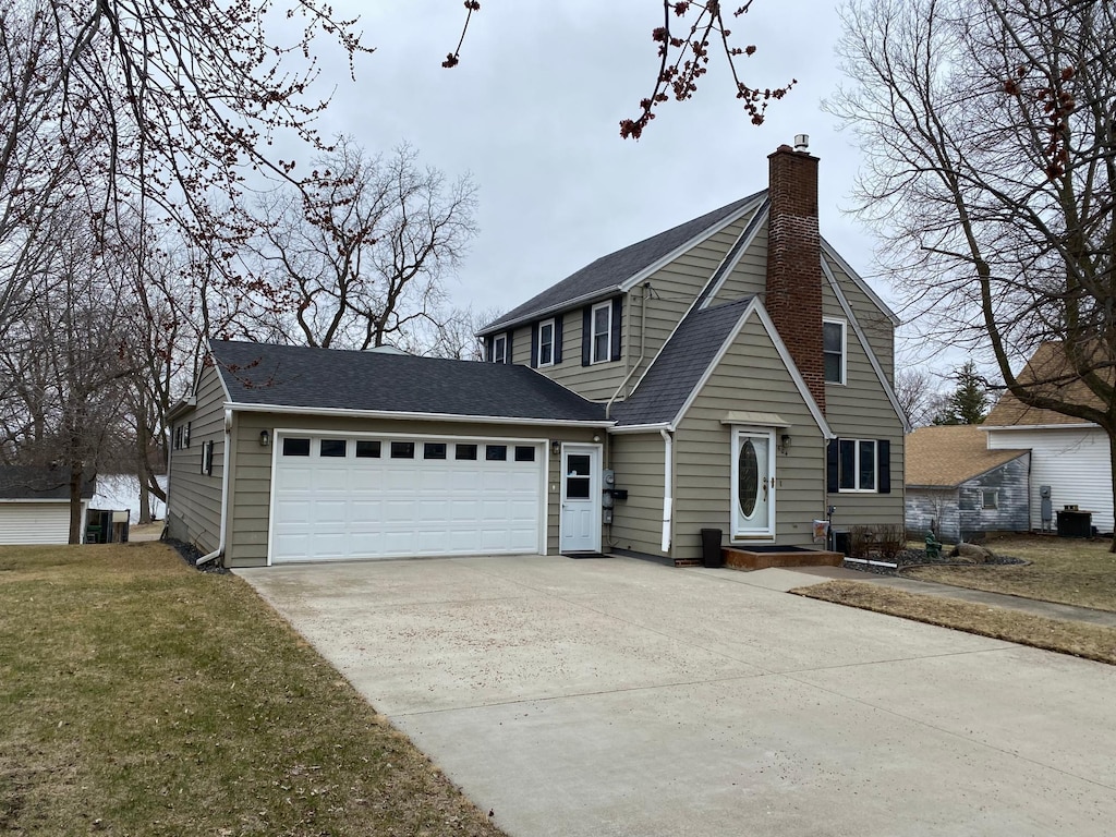view of front facade featuring driveway, a chimney, a front lawn, a garage, and central AC