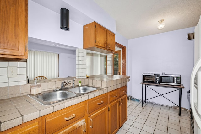 kitchen featuring tile counters, a sink, stainless steel microwave, and light tile patterned flooring