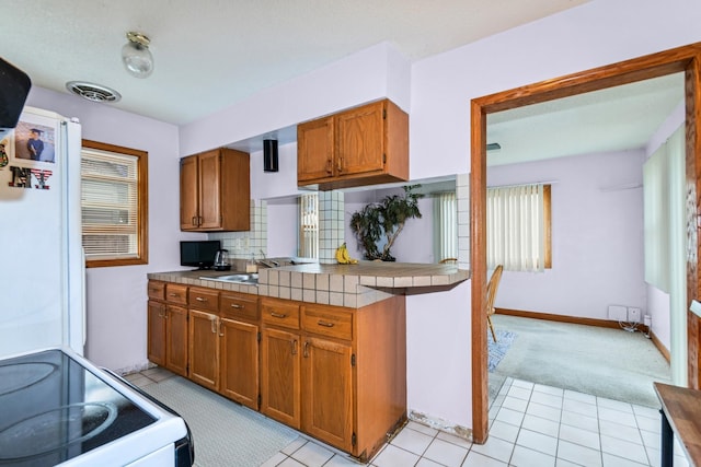 kitchen with visible vents, tasteful backsplash, brown cabinets, tile counters, and white appliances