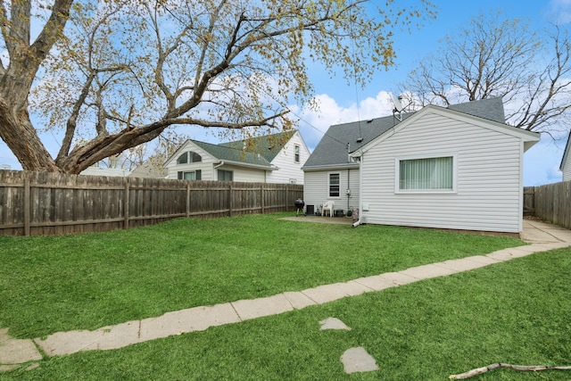 rear view of house with a fenced backyard, a lawn, and roof with shingles