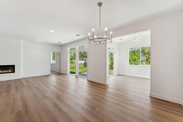 17729 Everest Ave, Lakeville, MN 55044 - unfurnished living room featuring wood finished floors, a glass covered fireplace, a chandelier, baseboards, and recessed lighting
