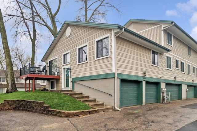 view of property exterior featuring a lawn, a wooden deck, an attached garage, and driveway