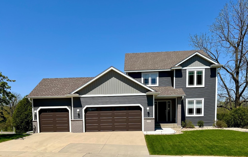 view of front of property with an attached garage, concrete driveway, a front yard, a shingled roof, and brick siding
