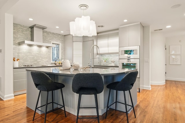 kitchen featuring wall chimney range hood, decorative backsplash, a kitchen breakfast bar, a sink, and recessed lighting