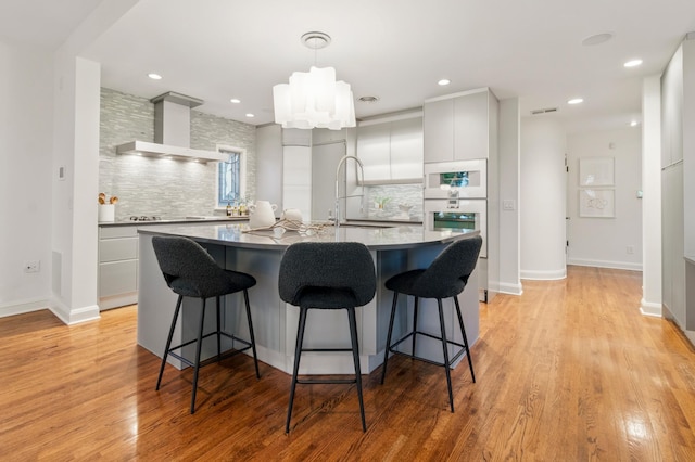 kitchen with wall chimney exhaust hood, a sink, tasteful backsplash, a kitchen bar, and recessed lighting
