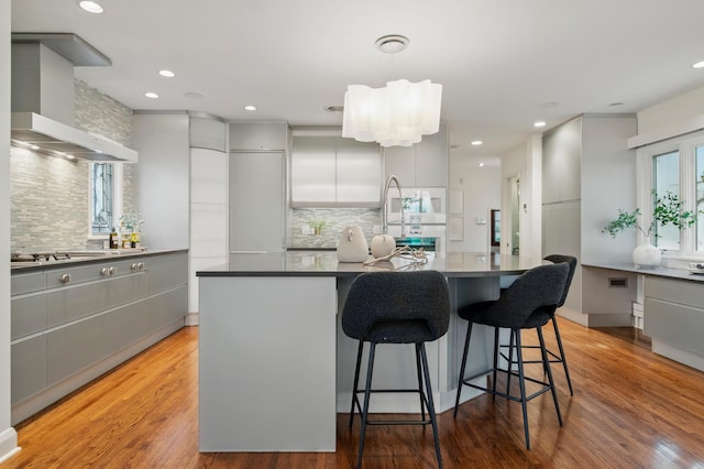 kitchen with wall chimney range hood, gray cabinets, tasteful backsplash, stainless steel gas stovetop, and recessed lighting