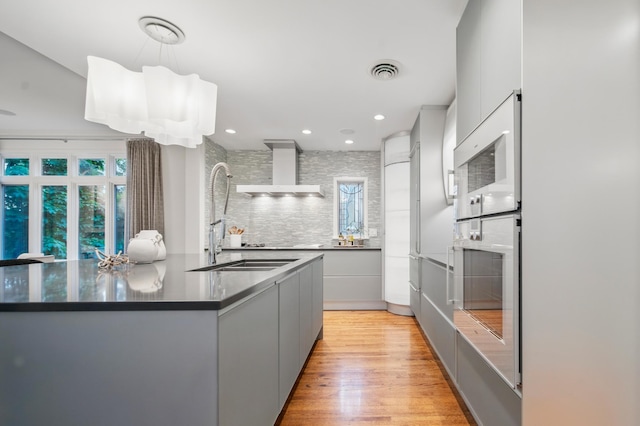 kitchen featuring white appliances, modern cabinets, wall chimney range hood, a sink, and dark countertops
