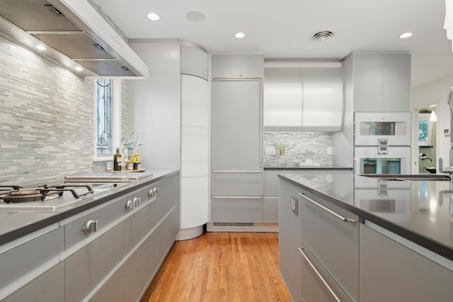 kitchen with exhaust hood, tasteful backsplash, gray cabinets, light wood-style flooring, and modern cabinets