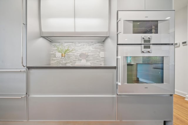 kitchen with oven, backsplash, white cabinets, modern cabinets, and built in fridge