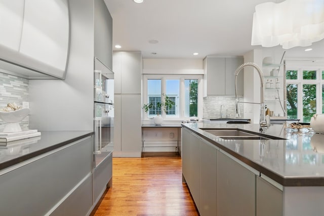 kitchen with a sink, tasteful backsplash, gray cabinetry, light wood finished floors, and modern cabinets
