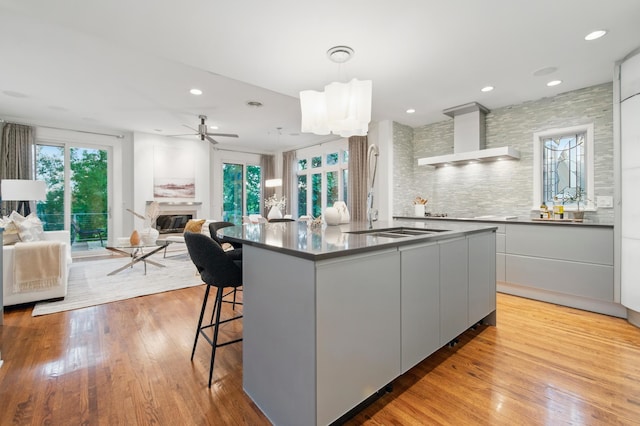 kitchen with modern cabinets, wall chimney range hood, dark countertops, open floor plan, and healthy amount of natural light
