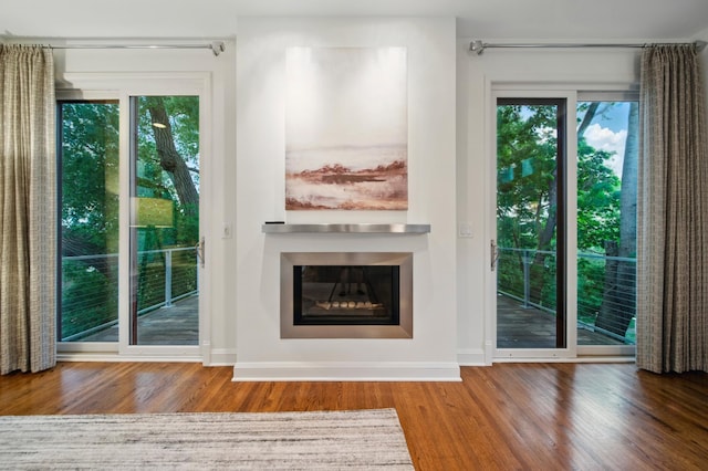 unfurnished living room featuring wood finished floors, baseboards, and a glass covered fireplace